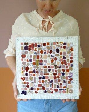 Dit werk heet Lavendel en honing en is 30x30 cm. Lavendel en honing is een werk met een Frans tintje. Annemieke houdt het werk vast in haar handen. Ze kijkt naar beneden naar het werk. Het kleurt mooi met het zachtroze bloesje.