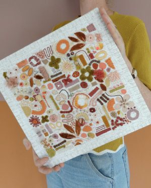 Dit werk heet Het gouden uurtje en is 30x30 cm. Het gouden uurtje is een warme textieltuin vol perzik-, honing- en goudtinten, geïnspireerd op het laatste avondlicht. Annemieke houd het werk iets schuin in haar handen.