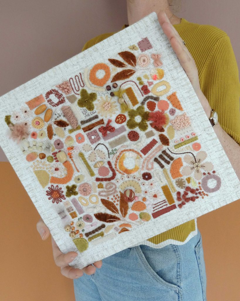 Dit werk heet Het gouden uurtje en is 30x30 cm. Het gouden uurtje is een warme textieltuin vol perzik-, honing- en goudtinten, geïnspireerd op het laatste avondlicht. Annemieke houd het werk iets schuin in haar handen.