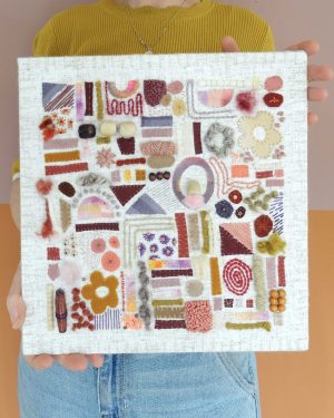 Dit werk heet Zaaien en oogsten en is 30x30 cm. Je ziet het werk van voren. Zaaien en oogsten is geïnspireerd op mijn moestuin, vol paadjes, zaadjes en vormen die samen een speelse plattegrond vormen. Annemieke heeft dit werk in haar handen.