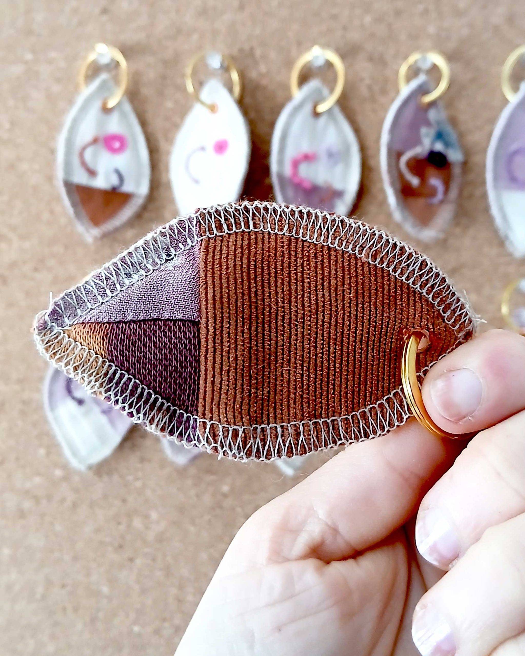 Achterkant van een handgemaakte sleutelhanger van hergebruikte stoffen. De sleutelhanger heeft een zachte textiele afwerking en maakt deel uit van de serie Knipoogjes. De achterkant heeft patchwork motief van oranje en paars. Dit is knipoog nummer 9.